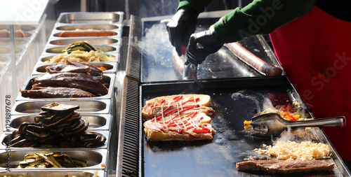 Tableau sur toile chef wearing gloves prepares sandwiches on the hot griddle with pork sausages an