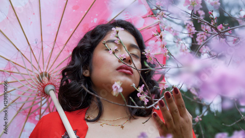 Beautiful woman smelling cherry blossoms under pink parasol