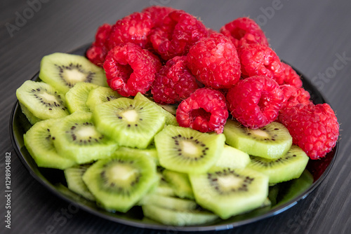 Kiwi and raspberry in a black plate. Peeled kiwi and raspberry.
