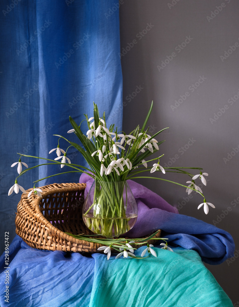 A Beautiful Arrangement of Elegant Snowdrops in a Glass Vase Surrounded by Colorful Textiles