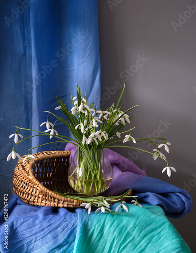 Obraz na płótnie A Beautiful Arrangement of Elegant Snowdrops in a Glass Vase Surrounded by Colorful Textiles w salonie