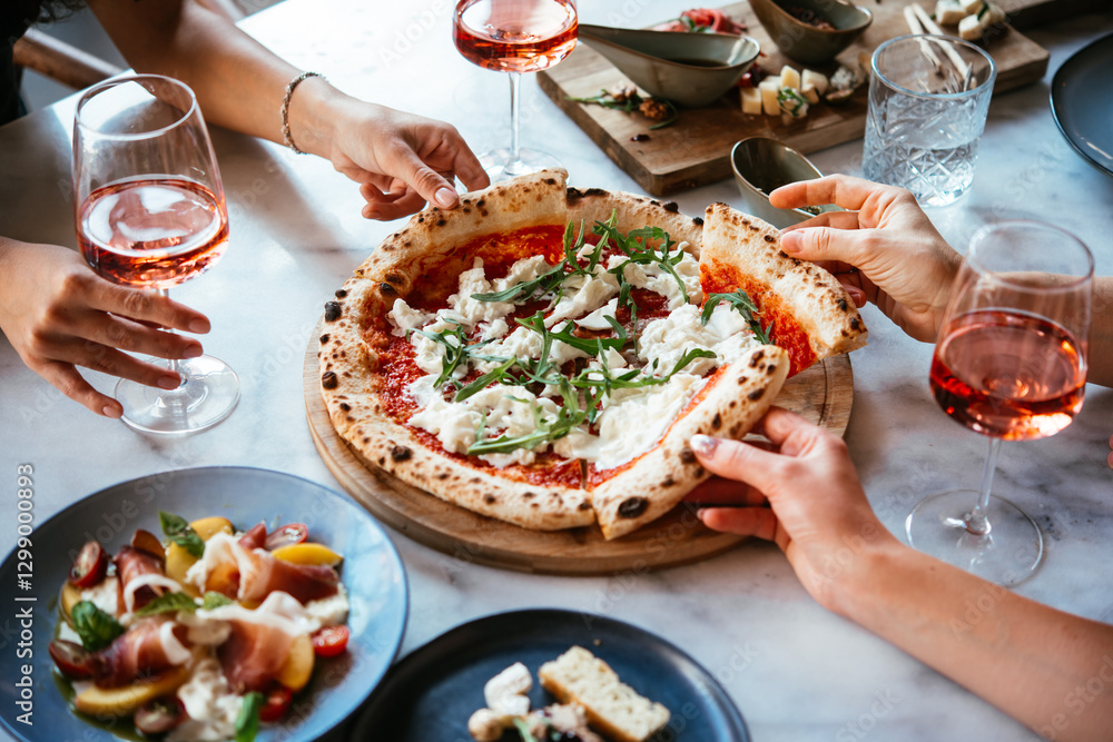 Friends enjoy a dinner party with pizza and rose wine in a bar or a restaurant.