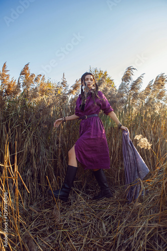 Obraz na płótnie Portrait of a beautiful brunette woman in a purple dress and jewelry standing in dry bushes outside in autumn w salonie