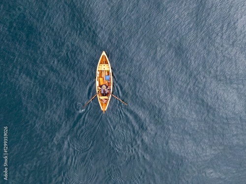 Фотография High-angle view of a person rowing a small wooden boat on calm water