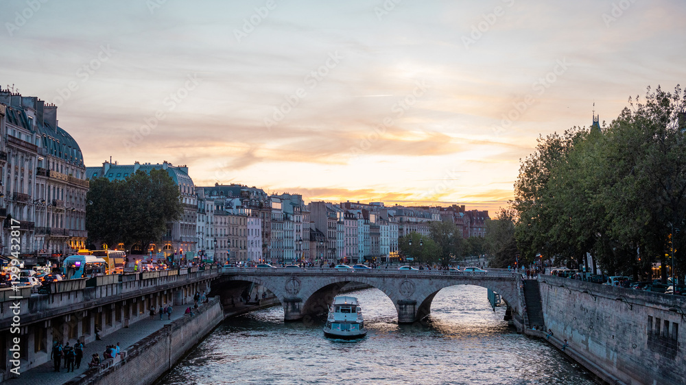 Lovely evening scene at the bridges over seine river in paris, with sun setting down in the distance. People and transport in direction of notre dame.
