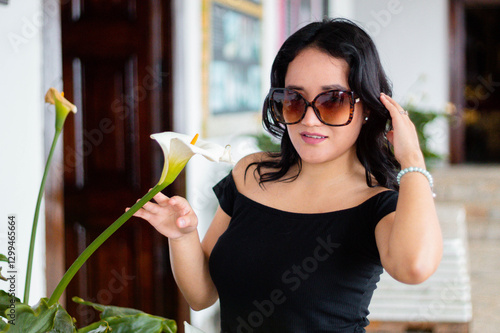 Retrato de mujer joven bonita con gafas belleza acariciando una flor blanca, elegancia y cuidado persona, estilo de vida saludable	