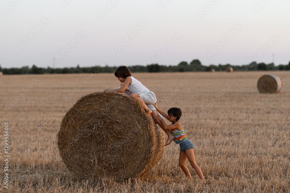Two siblings playing on a hay bale during sunset Two siblings playing on a hay bale during sunset