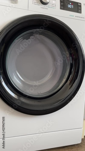 A front-loading washing machine spins clothes inside the drum during a laundry cycle. The digital display shows four minutes remaining until completion.