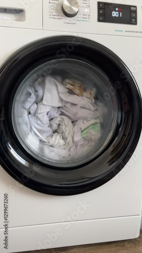 A front-loading washing machine spins clothes inside the drum during a laundry cycle. The digital display shows four minutes remaining until completion.