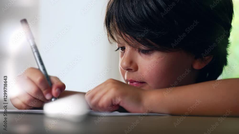Young boy concentrating on writing with a marker, carefully creating lines on the paper while seated at a desk, demonstrating focus and engagement Young boy concentrating on writing with a marker, carefully creating lines on the paper while seated at a desk, demonstrating focus and engagement