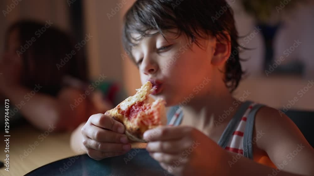 Young boy focusing on eating a slice of pizza, holding it with both hands, sitting at a table indoors, captured in a candid close-up moment as he enjoys his meal Young boy focusing on eating a slice of pizza, holding it with both hands, sitting at a table indoors, captured in a candid close-up moment as he enjoys his meal