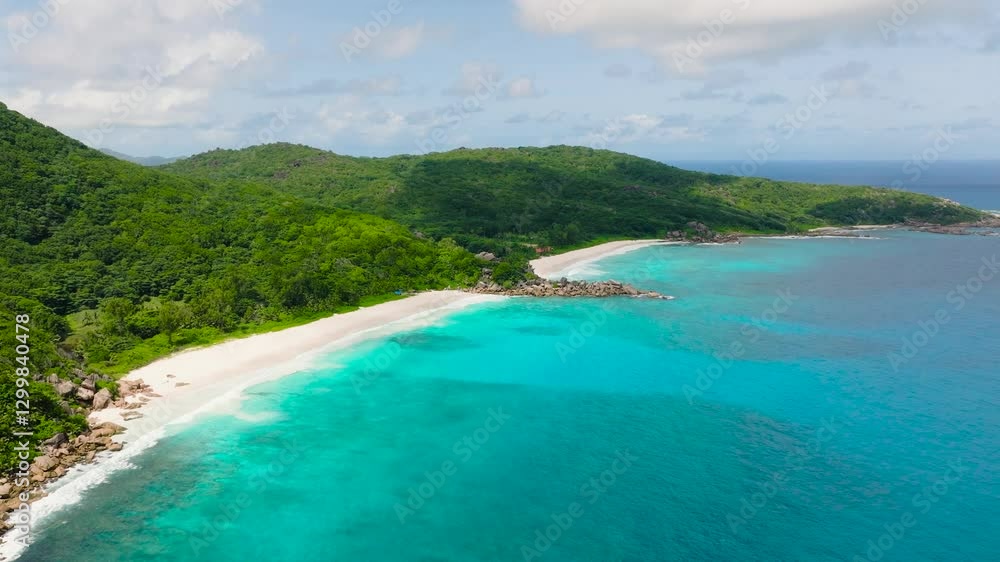 Mountain range covered in greenery overlooking a tropical beach with turquoise waters. La Digue, Seychelles. Mountain range covered in greenery overlooking a tropical beach with turquoise waters. La Digue, Seychelles.