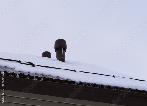 Vent stack with icicles on a snow-covered roof against sky background. Close-up