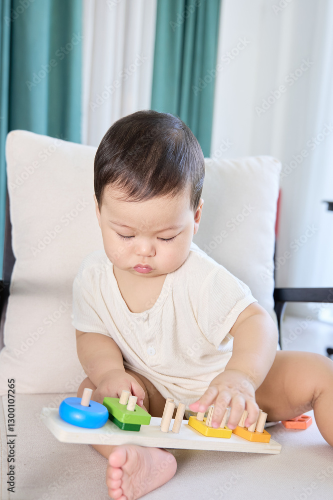 The baby is sitting on a couch and playing with toys, specifically a musical keyboard or xylophone.