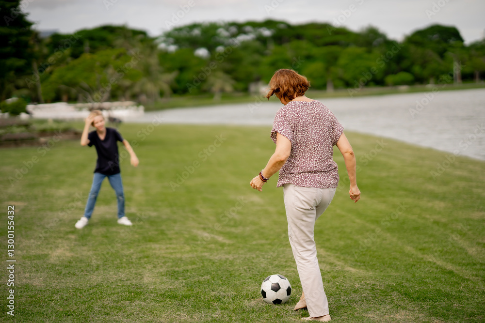 Grandmother play soccer with happy grandchild at summer outside park. Joyful senior retire kicking foot ball with preteen boy. Grandmother play soccer with happy grandchild at summer outside park. Joyful senior retire kicking foot ball with preteen boy.