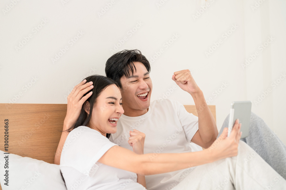 Excited couple celebrating a joyful moment while watching a screen in their cozy bedroom Excited couple celebrating a joyful moment while watching a screen in their cozy bedroom
