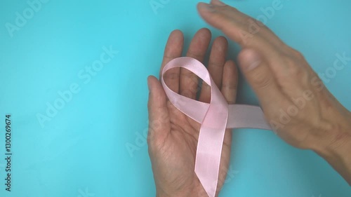 Footage video 4k. Hands holding pink ribbon on blue background. Breast cancer Awareness, male breast cancer disease, World Cancer Day. Healthcare or hospital and insurance concept.