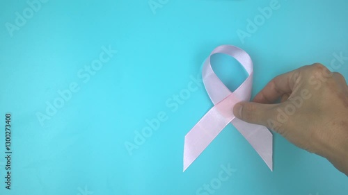Footage video 4k. Hands holding pink ribbon on blue background. Breast cancer Awareness, male breast cancer disease, World Cancer Day. Healthcare or hospital and insurance concept.