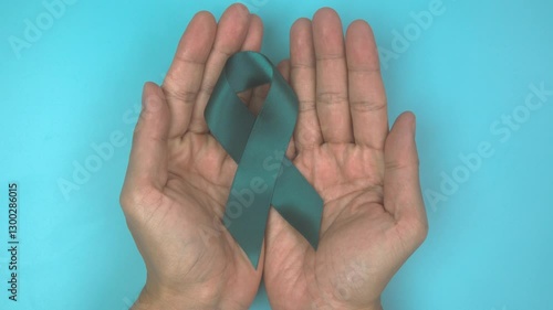 Footage video 4k. Hands holding teal ribbon on blue background.. Ovarian Cancer Awareness, Gynecological, Uterine Cancer, Vulvar Cancer, Panic Disorder, Post Traumatic Stress Disorder (PTSD).
