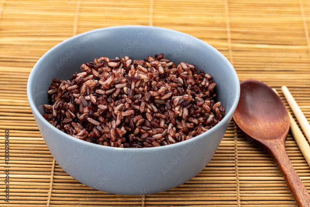 Healthy cooked brown rice mixed with riceberry in a grey ceramic bowl with a wooden spoon and bamboo chopsticks on the side. Healthy cooked brown rice mixed with riceberry in a grey ceramic bowl with a wooden spoon and bamboo chopsticks on the side.