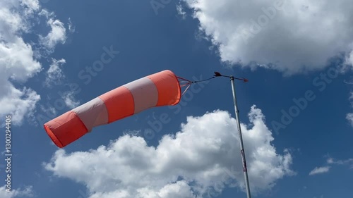 video of a wind sleeve to signal wind direction and intensity positioned at a parachute airfield, isolated against a blue sky with white clouds