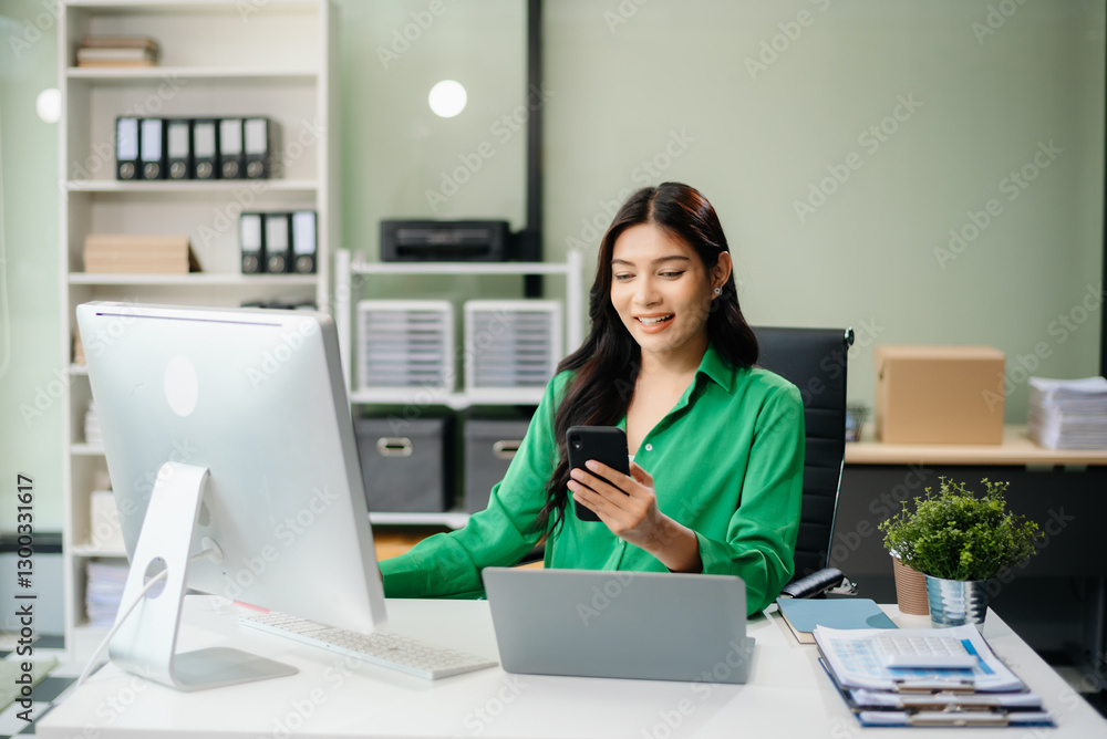 Asian woman using laptop and tablet while sitting at her working place. Concentrated Asian woman using laptop and tablet while sitting at her working place. Concentrated