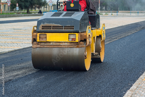 Road construction site with a roller compactor leveling fresh asphalt. Close-up on the machinery, highlighting the paving process.