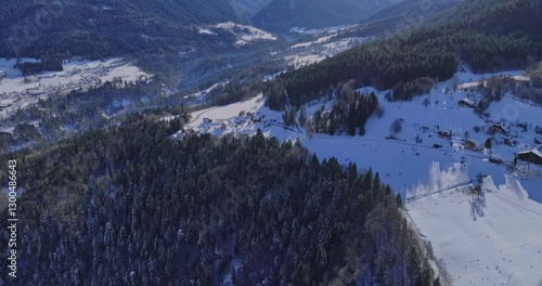 Aerial view of a snow-covered mountain village in winter, with forests and winding roads