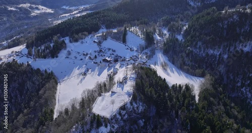 Aerial view of a snow-covered mountain village in winter, with forests and winding roads