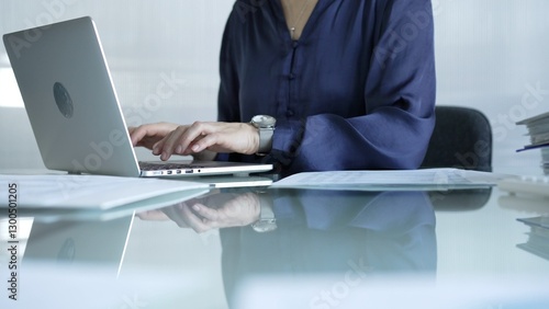 Obraz na płótnie Businesswoman in blue blouse typing on laptop at glass desk while sitting in bright office setting, close-up vie. Businesspeople concept w salonie