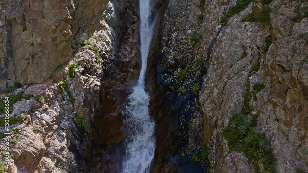 Small waterfall in mountain valley in mountains, close aerial drone view in sunny summer Kyrgyzstan. Clear weather and rugged terrain. Boom up camera movement,