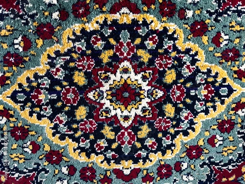 A close-up of a traditional woven carpet with an intricate floral pattern, featuring deep red, gold, green, and black tones. This classic Russian-style rug showcases detailed ornamentation, a rich