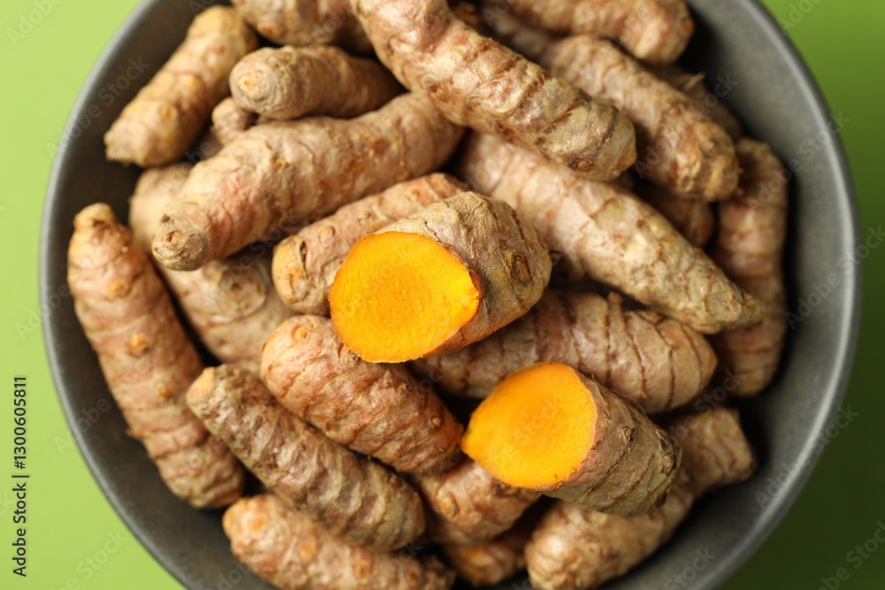 Tumeric rhizomes in bowl on green background, top view Tumeric rhizomes in bowl on green background, top view
