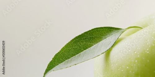 A green apple accompanied by a green leaf rests on a white surface