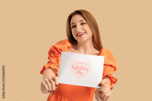 Happy young woman holding greeting card with text HAPPY VALENTINE'S DAY on beige background