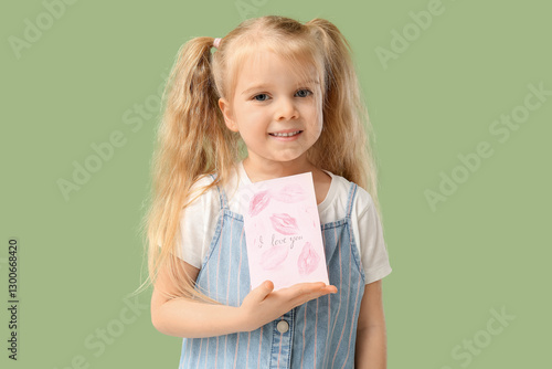 Cute little girl holding greeting card with text I LOVE YOU and kiss marks on green background. Valentine's Day celebration