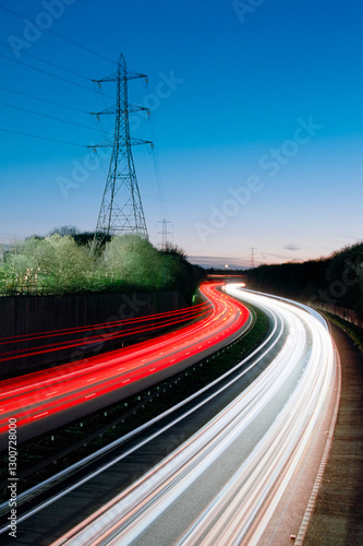 Light trails from moving traffic on a road against a blue sky depicting high speed, commute, rush hour, travel