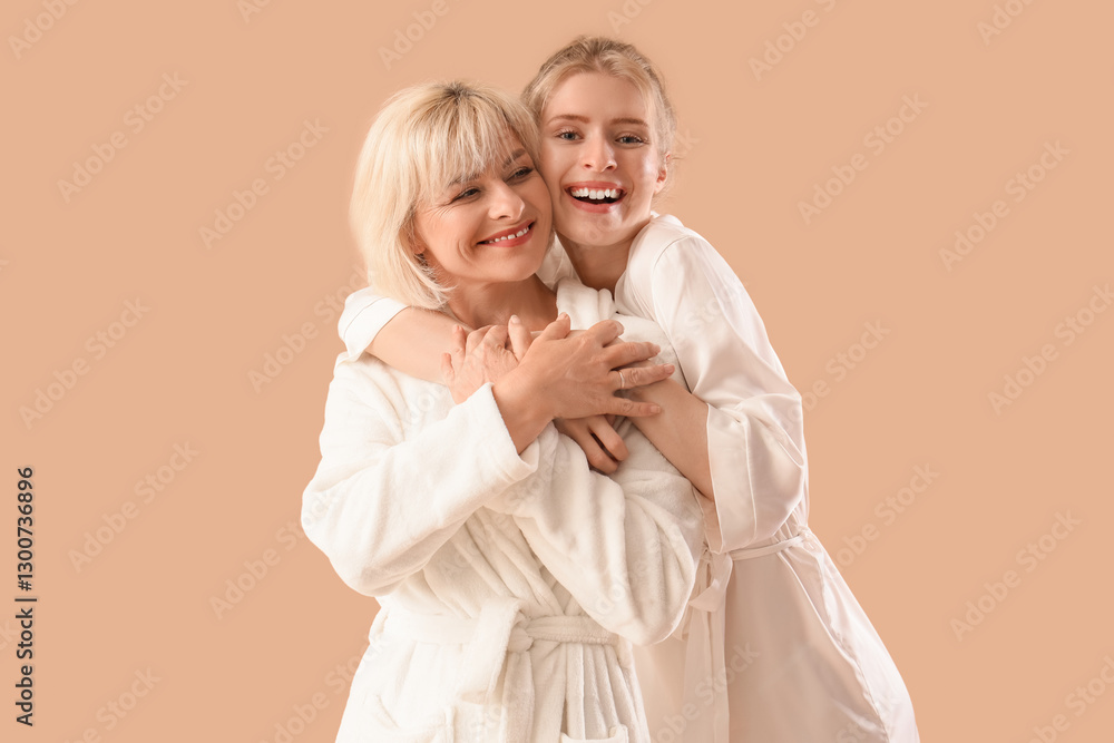 Happy young woman and her mother in bathrobes hugging on beige background Happy young woman and her mother in bathrobes hugging on beige background