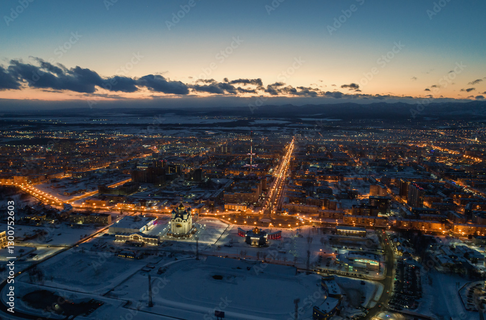 Obraz premium Urban landscape illuminated by evening lights showcasing Yuzhno-Sakhalinsk city at dusk in cold winter conditions.