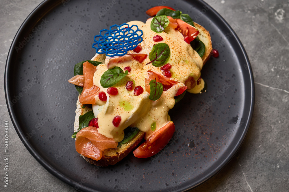 Delicious open-faced sandwich with smoked salmon, creamy sauce, fresh spinach, vibrant pomegranate seeds on dark plate, gourmet meal concept