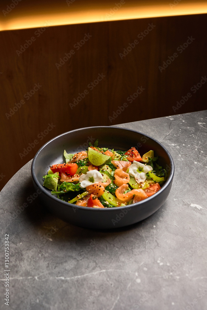 Salmon, avocado, and tomato salad with lime in black bowl on marble table, healthy eating concept