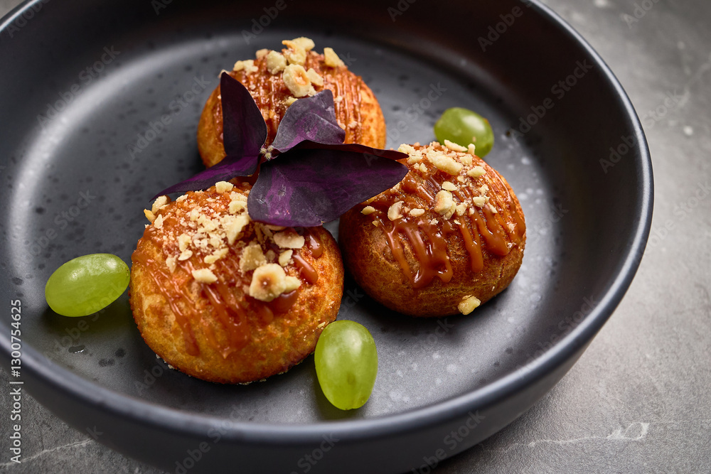 Delicious profiteroles with caramel drizzle, nuts, grapes, with dark leaf garnish on plate, gourmet dessert presentation concept