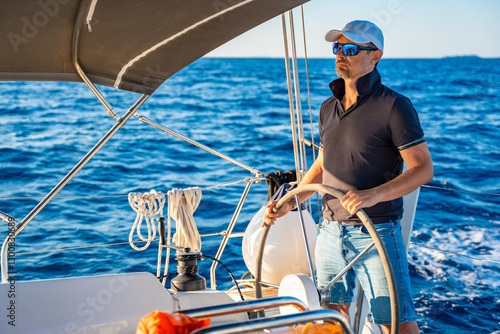 Konstfotografi Young man captain stands at the helm and controls a sailboat during a journey by