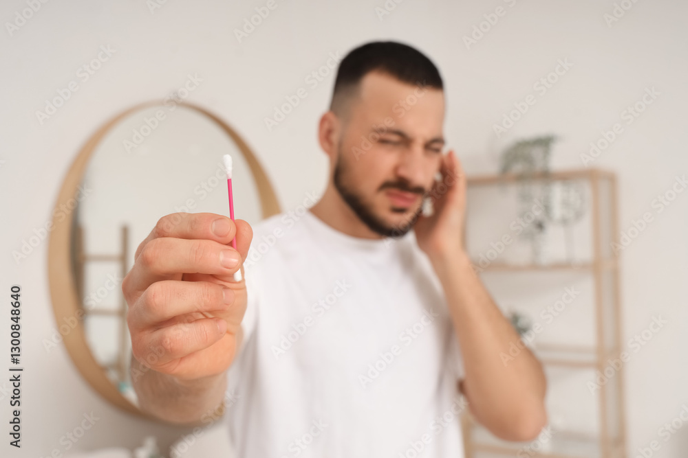 Young man feeling discomfort while cleaning ears with cotton bud in bathroom Young man feeling discomfort while cleaning ears with cotton bud in bathroom