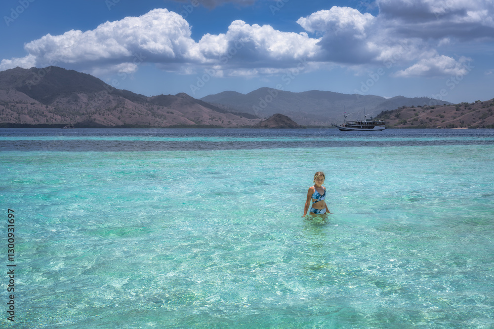 A serene and tranquil beach adorned with crystalclear waters, where a young girl leisurely strolls through, complemented by picturesque mountains in the background, Komodo, Indonesia
