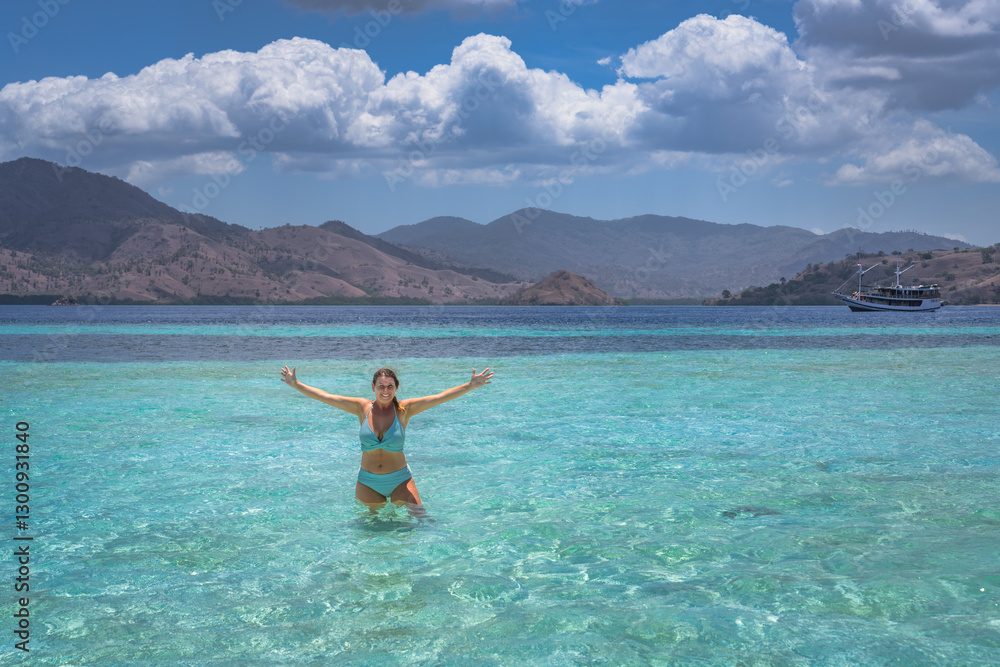 A truly joyful, unforgettable moment at the beautiful beach, showcasing clear turquoise waters alongside a stunning mountain backdrop beneath a bright blue sky, Komodo, Indonesia