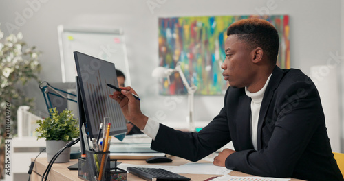 Handsome dark-skinned man, corporate office worker spends morning in front of computer, points at screen, counts, ponders, checks correctness of graphs, completes data