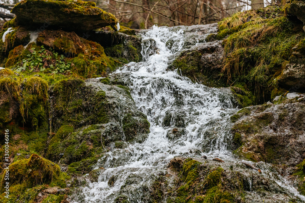 Naklejka premium A beautiful multi-tiered waterfall flows over moss-covered rocks in a forest setting. The long exposure captures the smooth movement of the water, creating a peaceful and serene natural scene.