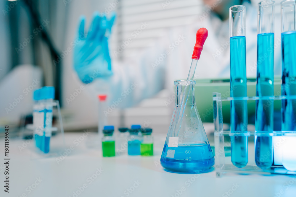 Lab table with a blue beaker and a red dropper. The table is cluttered with various glassware and chemicals