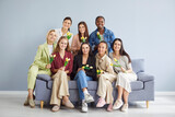 Group of happy smiling diverse women sitting on sofa together and holding yellow tulip flower bouquets. Joyful stylish multinational ladies looking at camera and celebrating International Women Day.